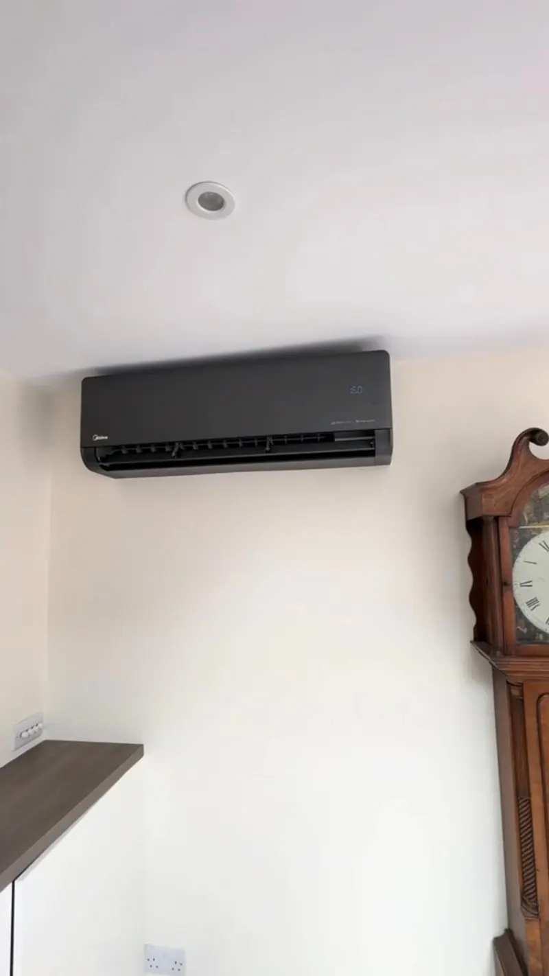 Matte black indoor air conditioning unit on a white wall beside a grandfather clock in a period room