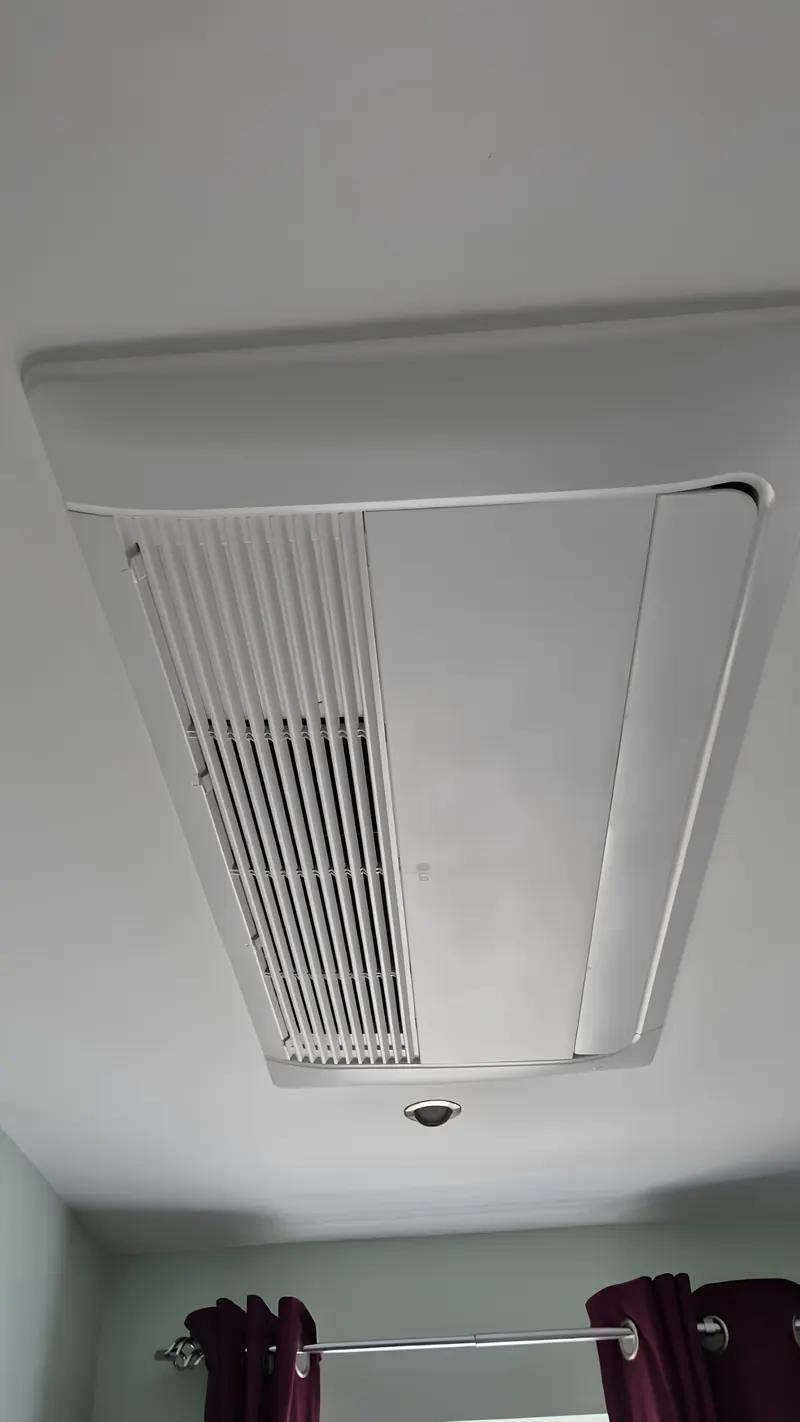 Ceiling cassette air conditioning unit recessed into a white ceiling next to a downlight