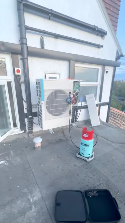 Outdoor unit on a flat roof beside patio doors with refrigerant cylinder and gauges during commissioning