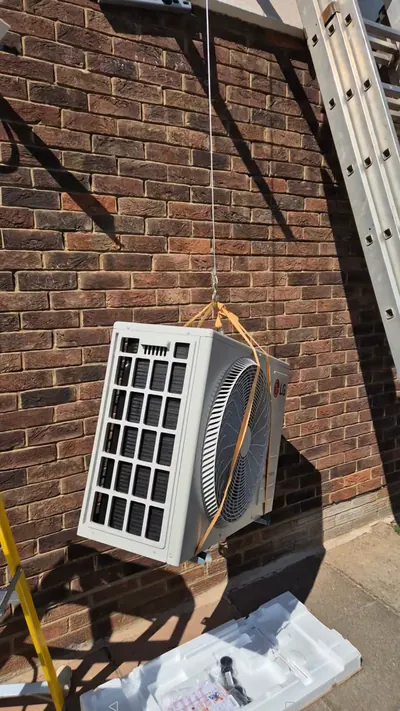 Outdoor unit suspended on lifting straps against a brick wall during installation