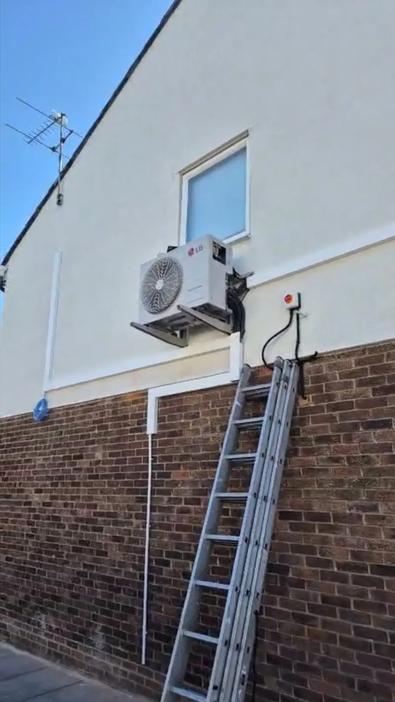 Air conditioning outdoor unit mounted high on a rendered rear wall away from the highway